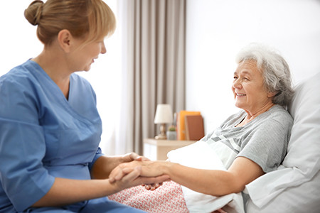 Care Services helping senior woman sit up in bed, smiling