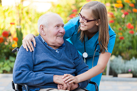 Caregiver helping elderly man in a wheelchair smiling