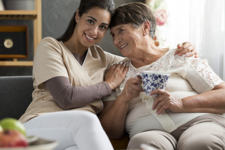 Caring person and happy elderly woman drinking tea at home