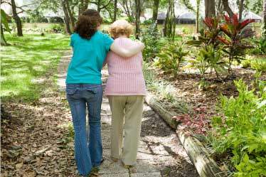 Caregiver helping an elderly woman walk on garden path