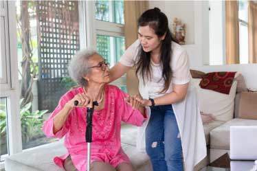 Caregiver helping elderly woman with cane stand up in our Residential Care Homes