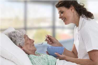 Hospice nurse smiling, while feeding patient soup