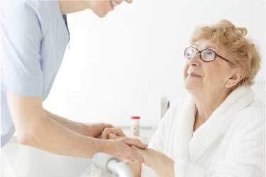 Hospice nurse holding seated senior woman's hands