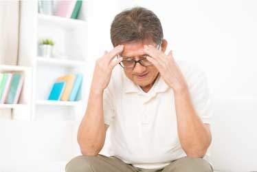 Man seated, hands to forehead, worried about memory care costs