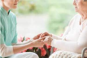 Nurse holding hands of disabled elderly woman in a wheelchair