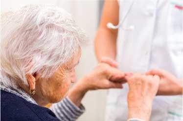 Elderly woman seated, holding nurses hands