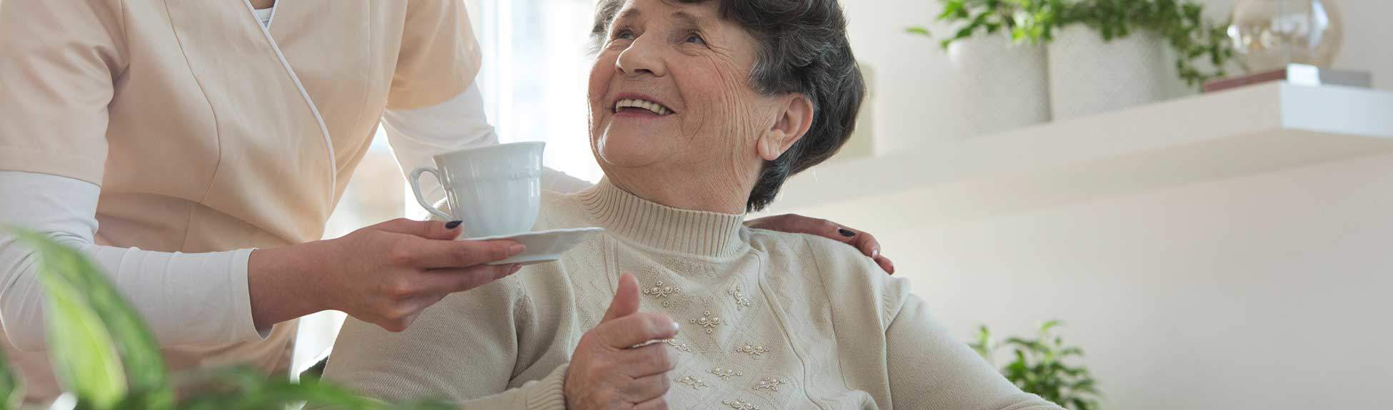 Premier Assisted Living Nurse serving tea to senior woman smiling