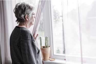 Senior woman appearing depressed, looking out her window of assisted living facility